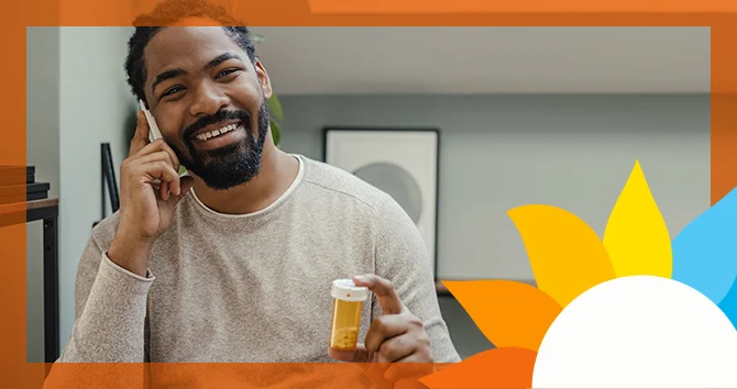 a smiling man speaks on the phone holding a pill bottle