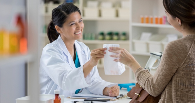 a smiling pharmacist hands out a prescription